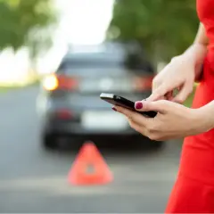 Kobieta w czerwonej sukience używa telefonu komórkowego przy awaryjnym samochodzie z trójkątem ostrzegawczym.