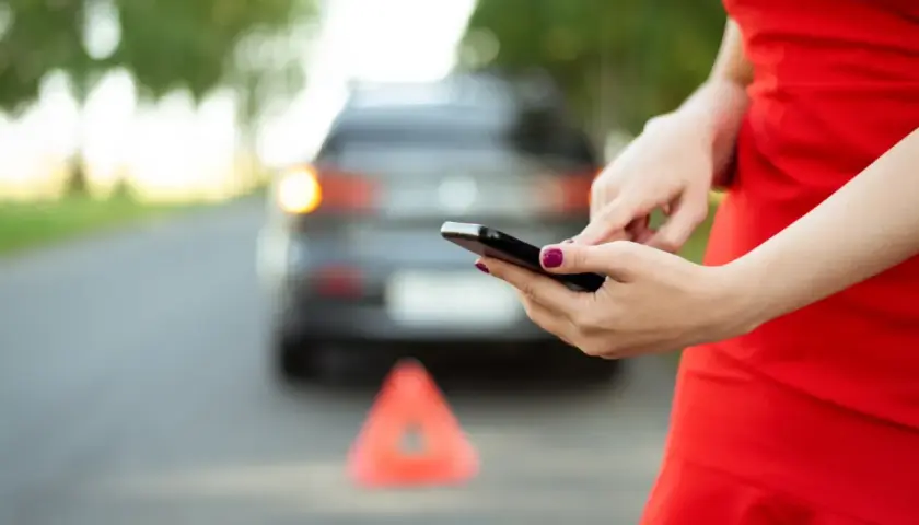Kobieta w czerwonej sukience używa telefonu komórkowego przy awaryjnym samochodzie z trójkątem ostrzegawczym.