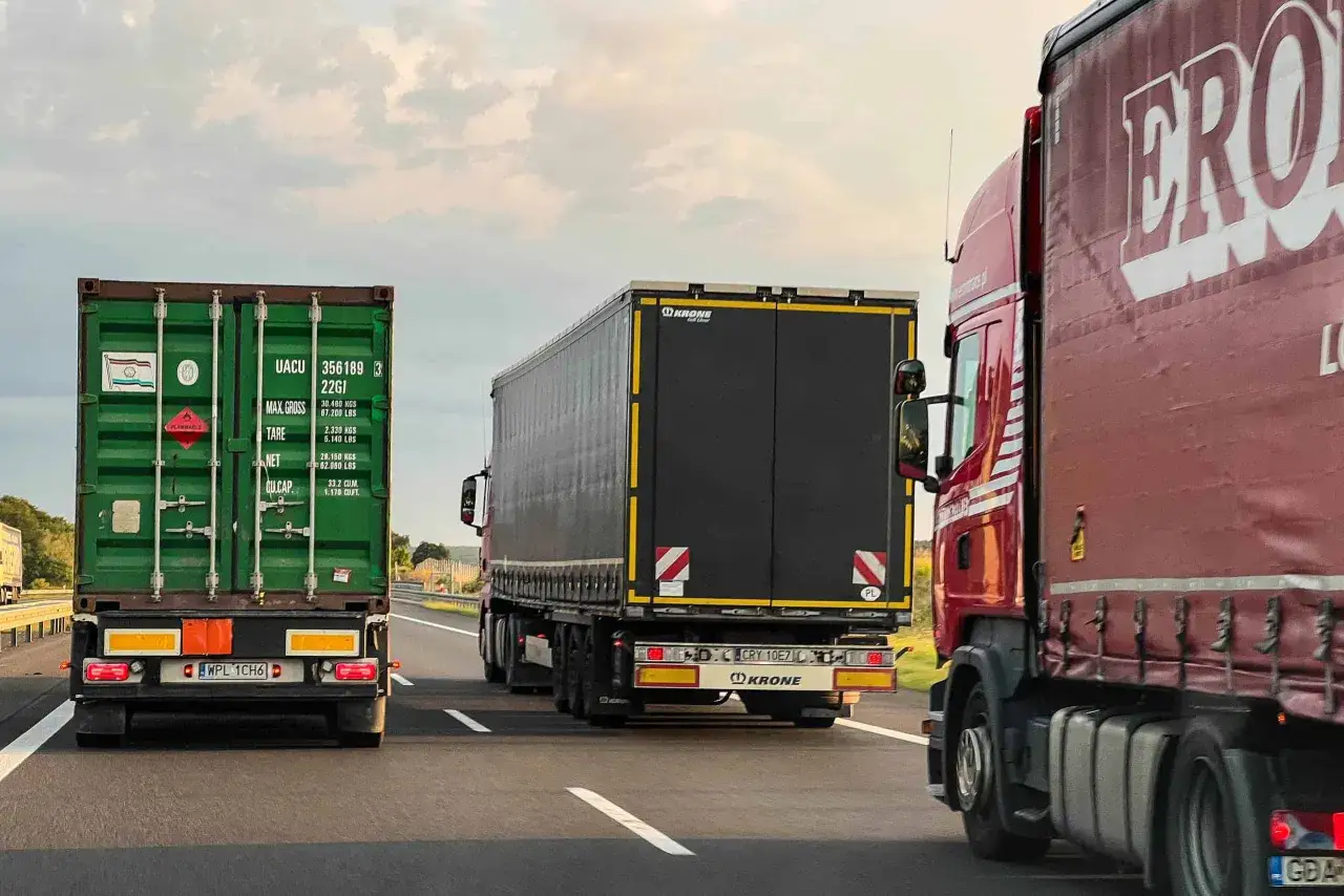 Trzy ciężarówki na autostradzie. Jedna z zielonym kontenerem, druga z czarną naczepą Krone, trzecia czerwona z logo ERO. Zakaz wyprzedzania ciężarówek od kiedy?